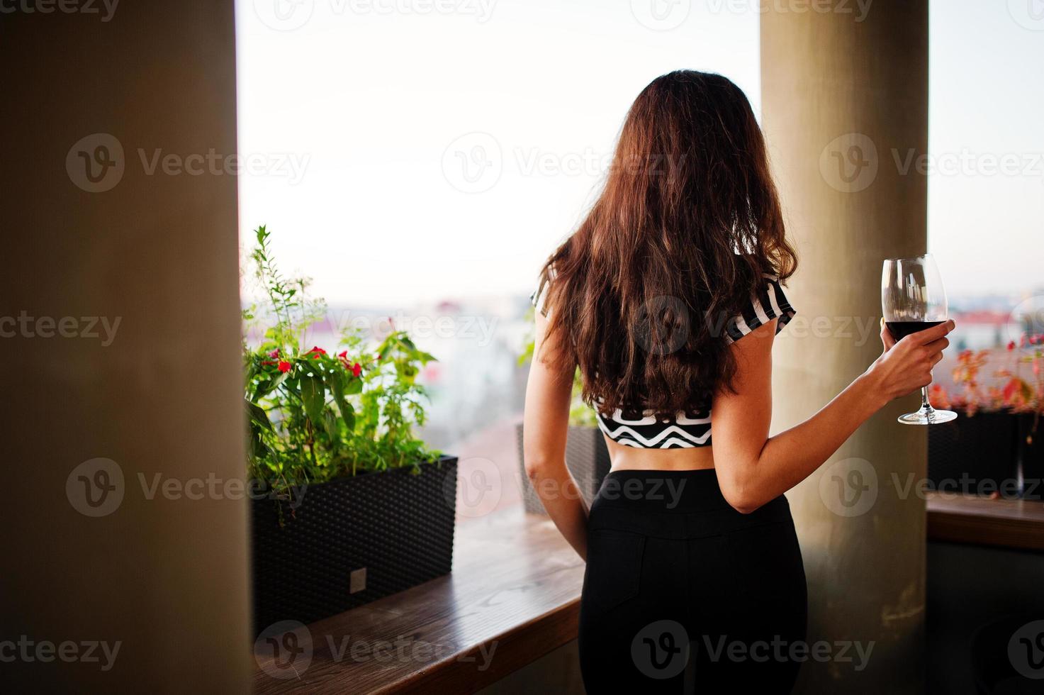 parte posteriore di una giovane donna riccia e sexy che si gode il vino in un bar. foto