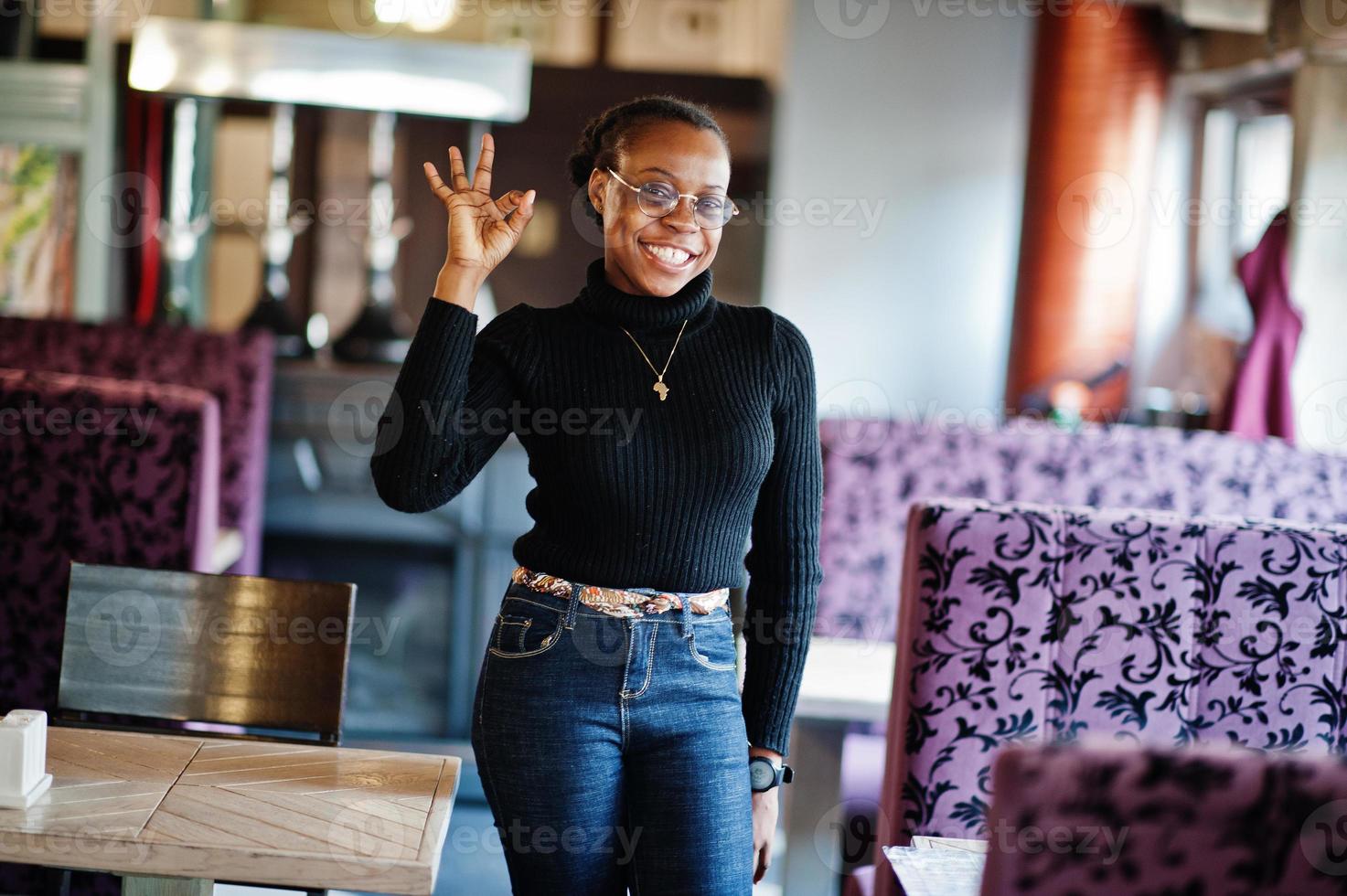 donna africana in maglione nero posata al bar e mostra a mano il segno giusto. foto