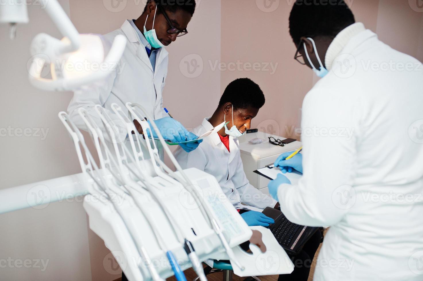 tre medici maschi afroamericani che lavorano con il laptop, discutendo con i colleghi in clinica odontoiatrica. foto