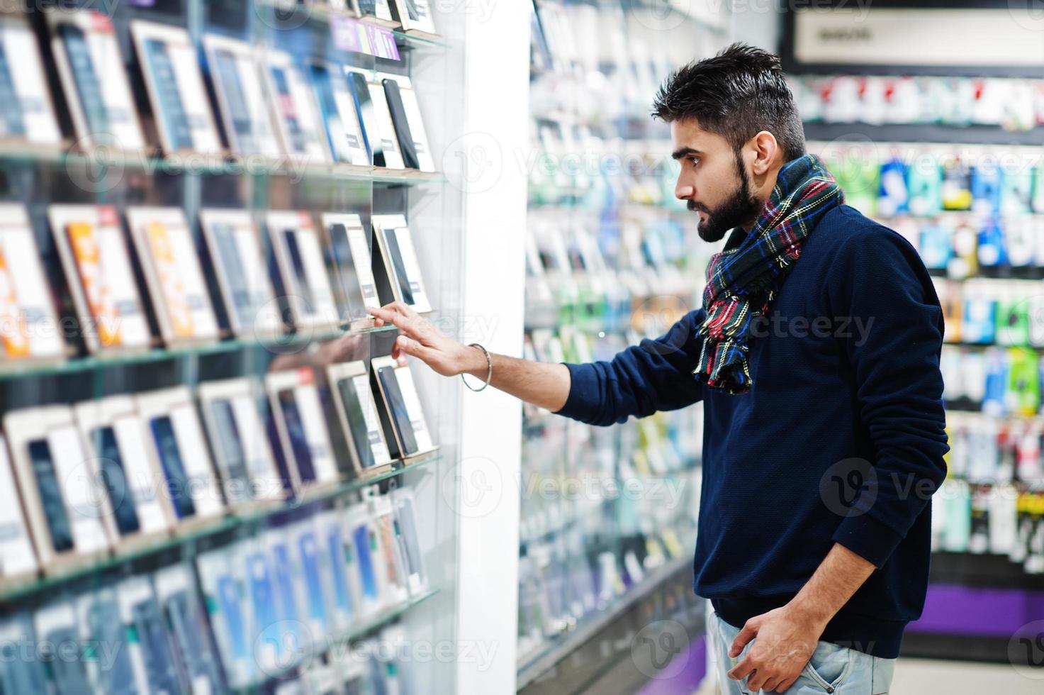 l'acquirente del cliente dell'uomo della barba indiana presso il negozio di telefoni cellulari sceglie il suo nuovo smartphone. concetto di popoli e tecnologie dell'Asia meridionale. negozio di cellulari. foto