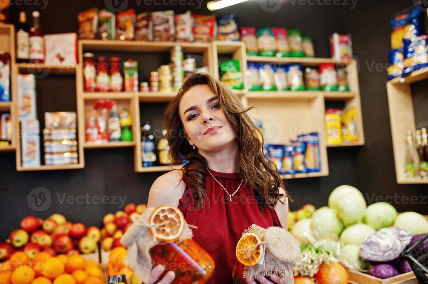 ragazza in rosso che tiene marmellata in un barattolo sul negozio di frutta. foto
