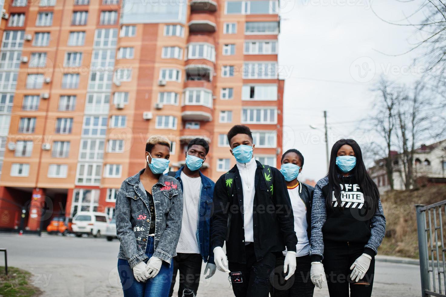 gruppo di adolescenti africani amici contro una strada vuota con edificio che indossa maschere mediche proteggere da infezioni e malattie quarantena del virus del coronavirus. foto