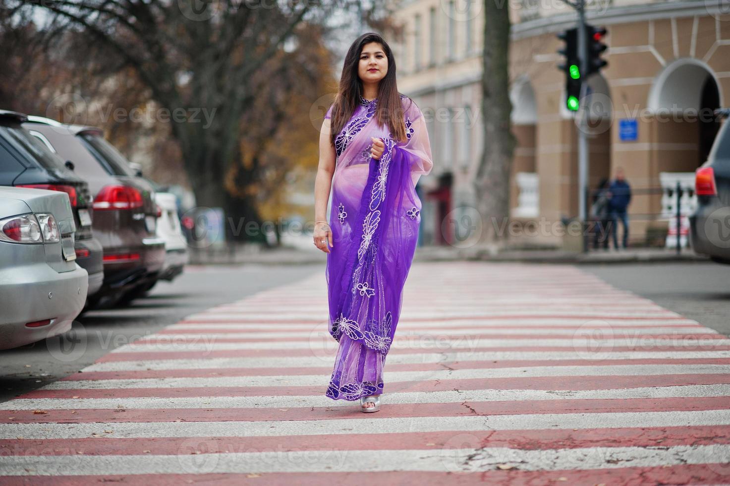 ragazza indiana indù al tradizionale saree viola posato in strada, camminando al passaggio pedonale. foto