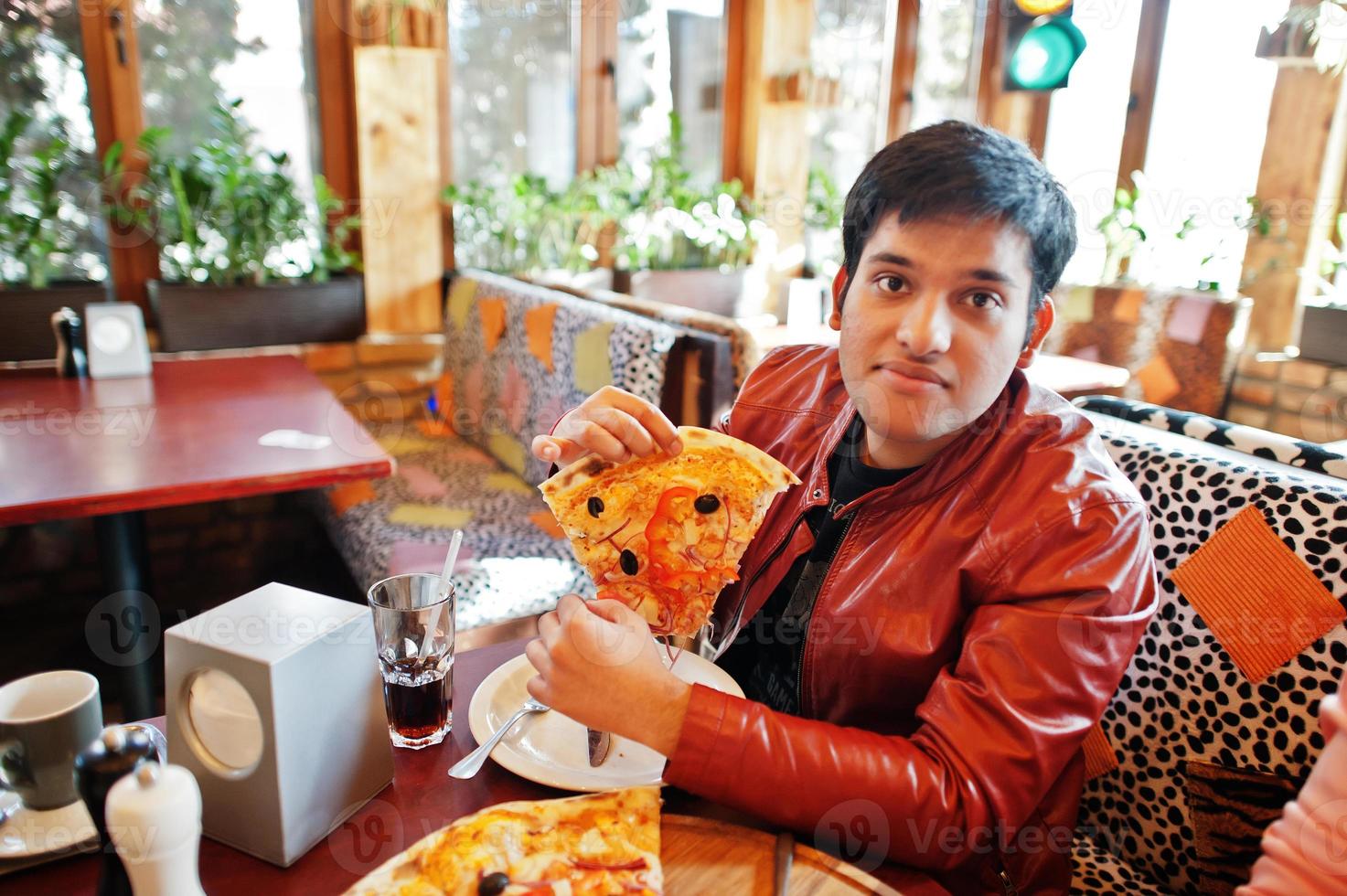 uomo asiatico che mangia pizza durante la festa in pizzeria. ragazzo che mangia cibo italiano e si siede sul divano. foto