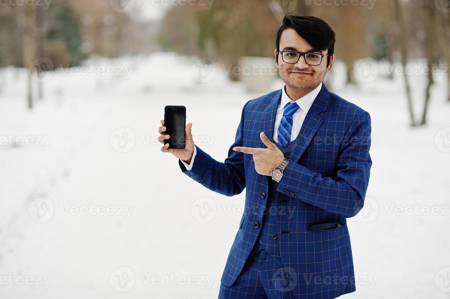 elegante uomo d'affari indiano in giacca e occhiali poste in una giornata invernale all'aperto, con il telefono cellulare a portata di mano. foto