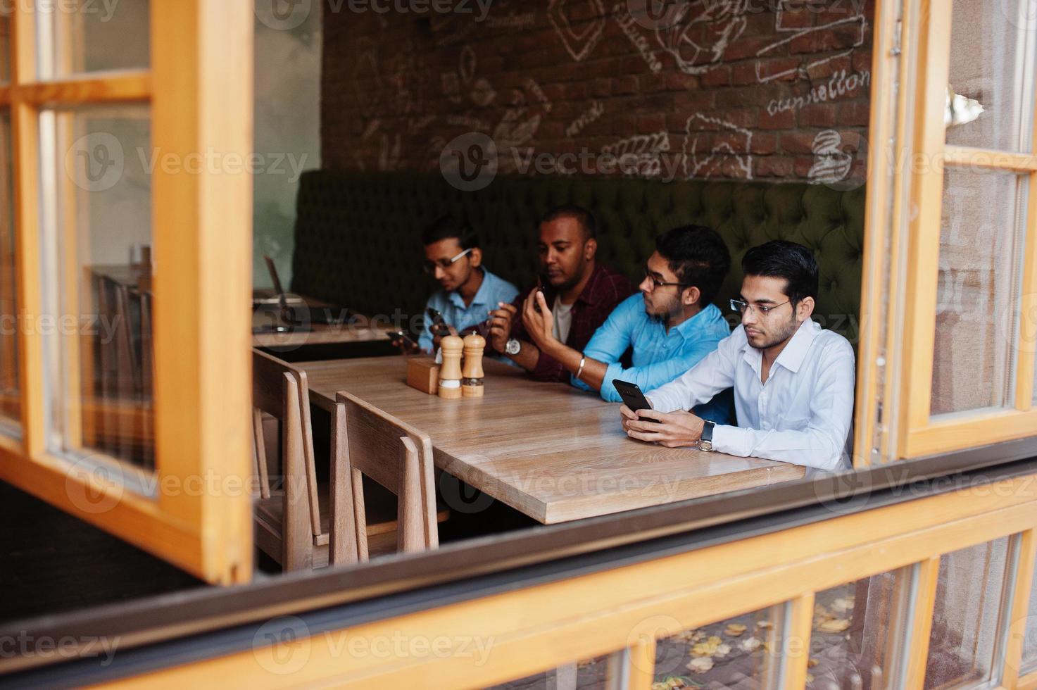 un gruppo di quattro uomini del sud asiatico poste alla riunione di lavoro nella caffetteria. gli indiani lavorano insieme usando vari gadget, conversando. foto