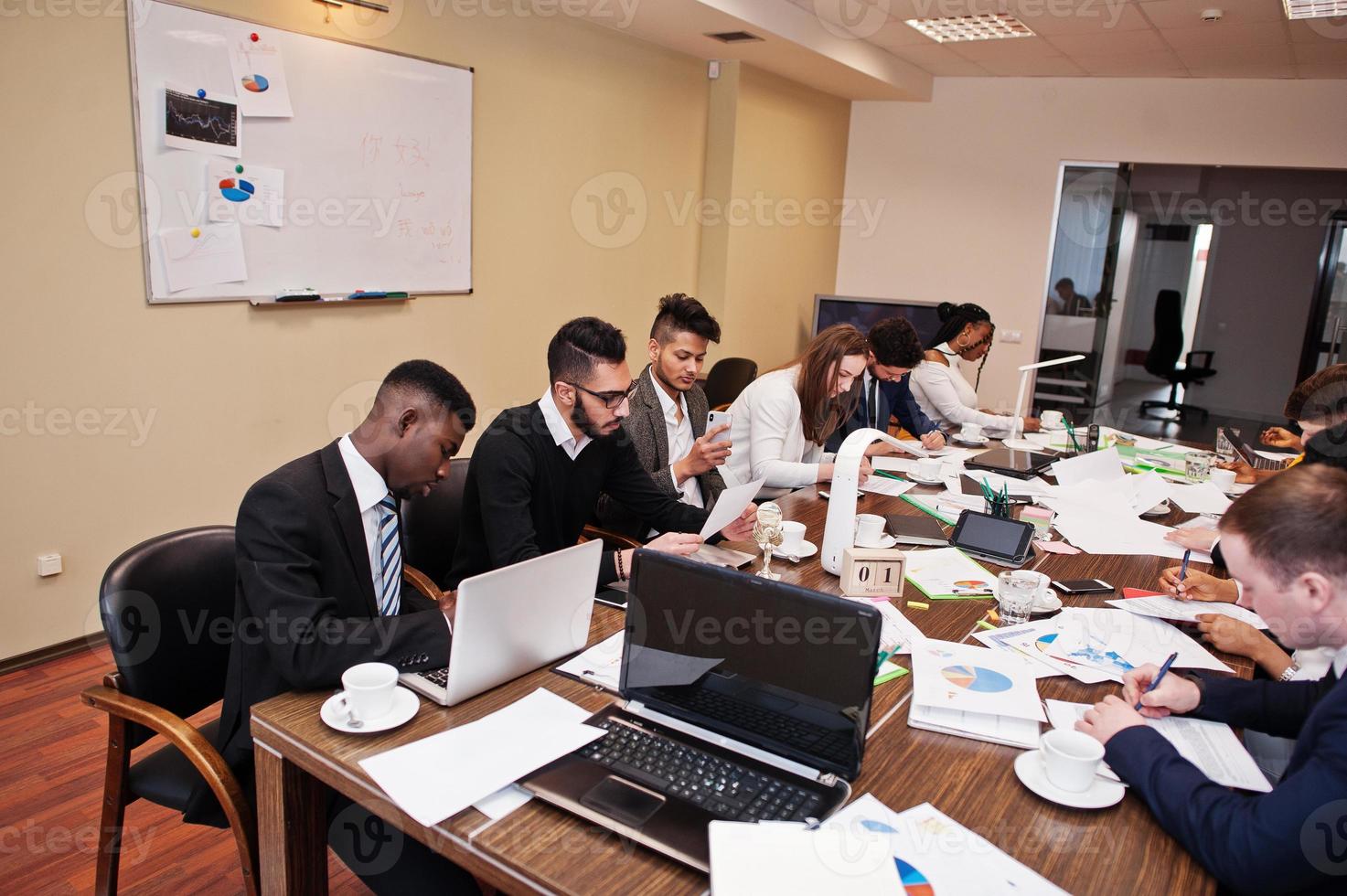 team aziendale multirazziale che si rivolge alla riunione attorno al tavolo della sala riunioni, lavora insieme e scrive qualcosa sui fogli. foto