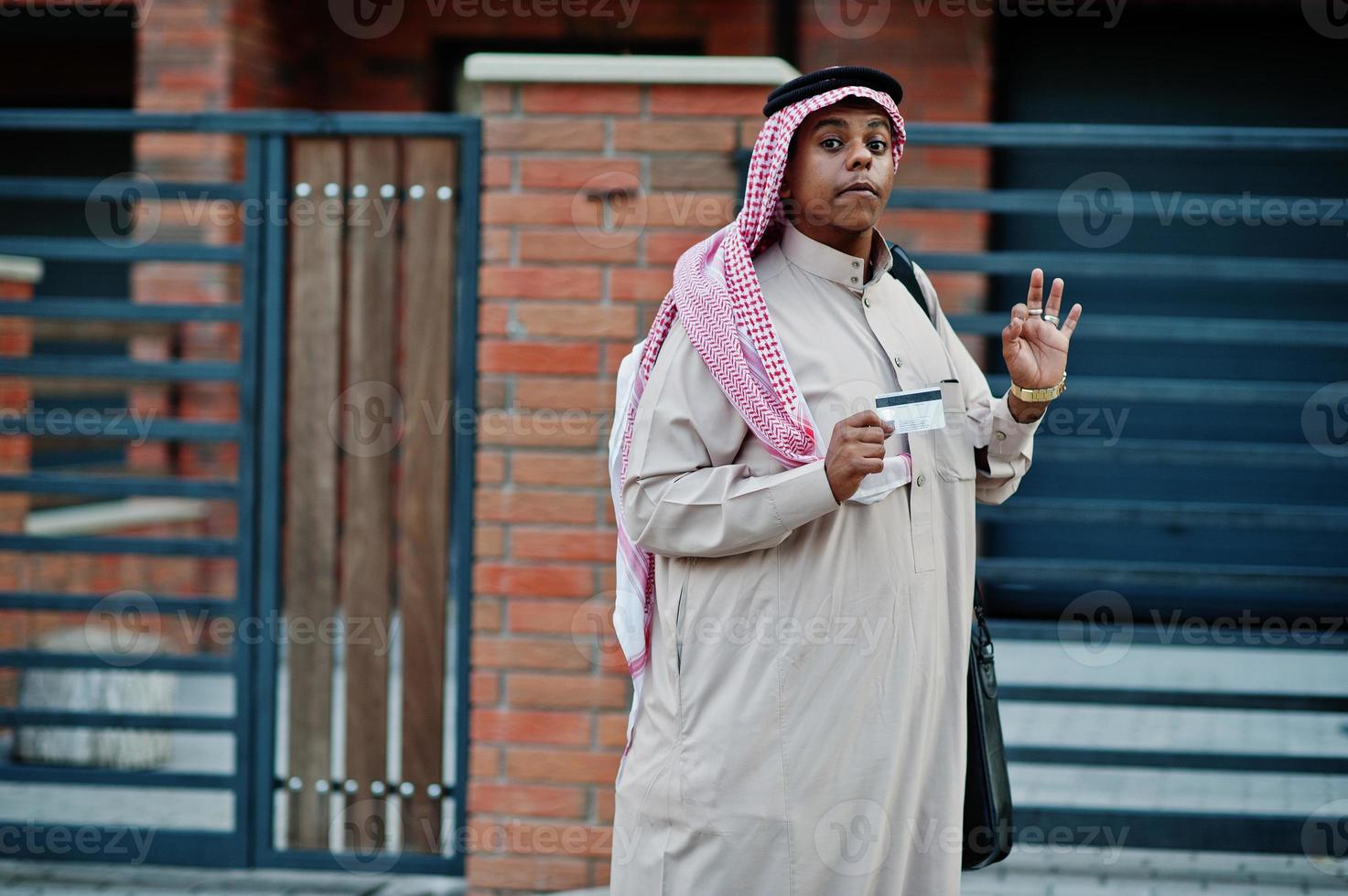 uomo d'affari arabo mediorientale posato su strada contro un edificio moderno con borsa nera e carta di credito a portata di mano. foto