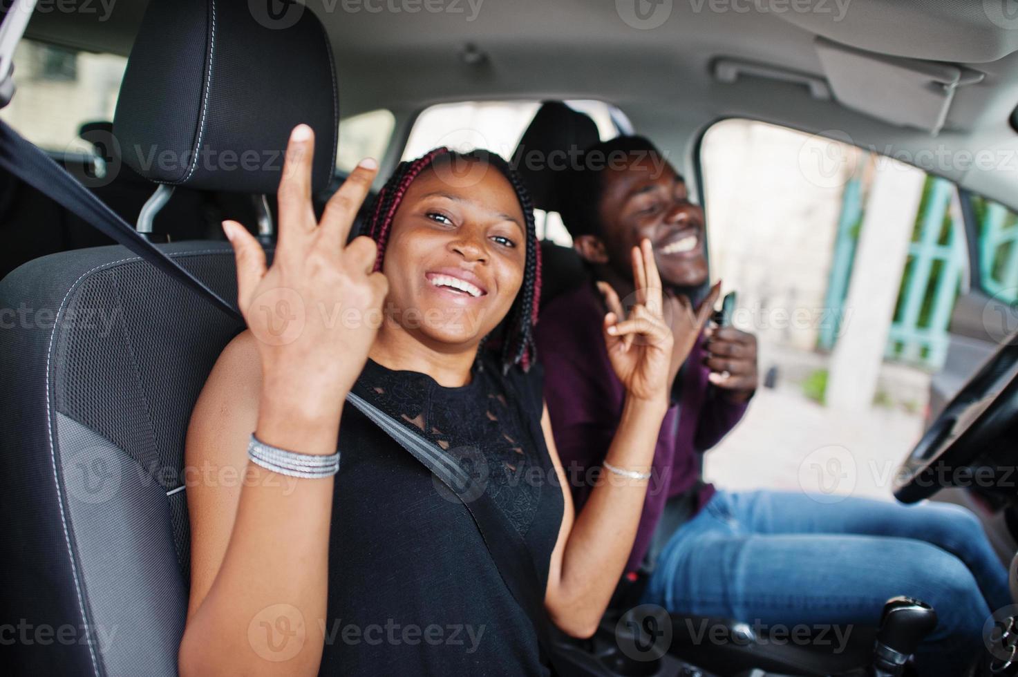 bella giovane coppia afroamericana seduta sui sedili dei passeggeri anteriori mentre un bell'uomo guida un'auto. ascoltare musica e ballare. foto