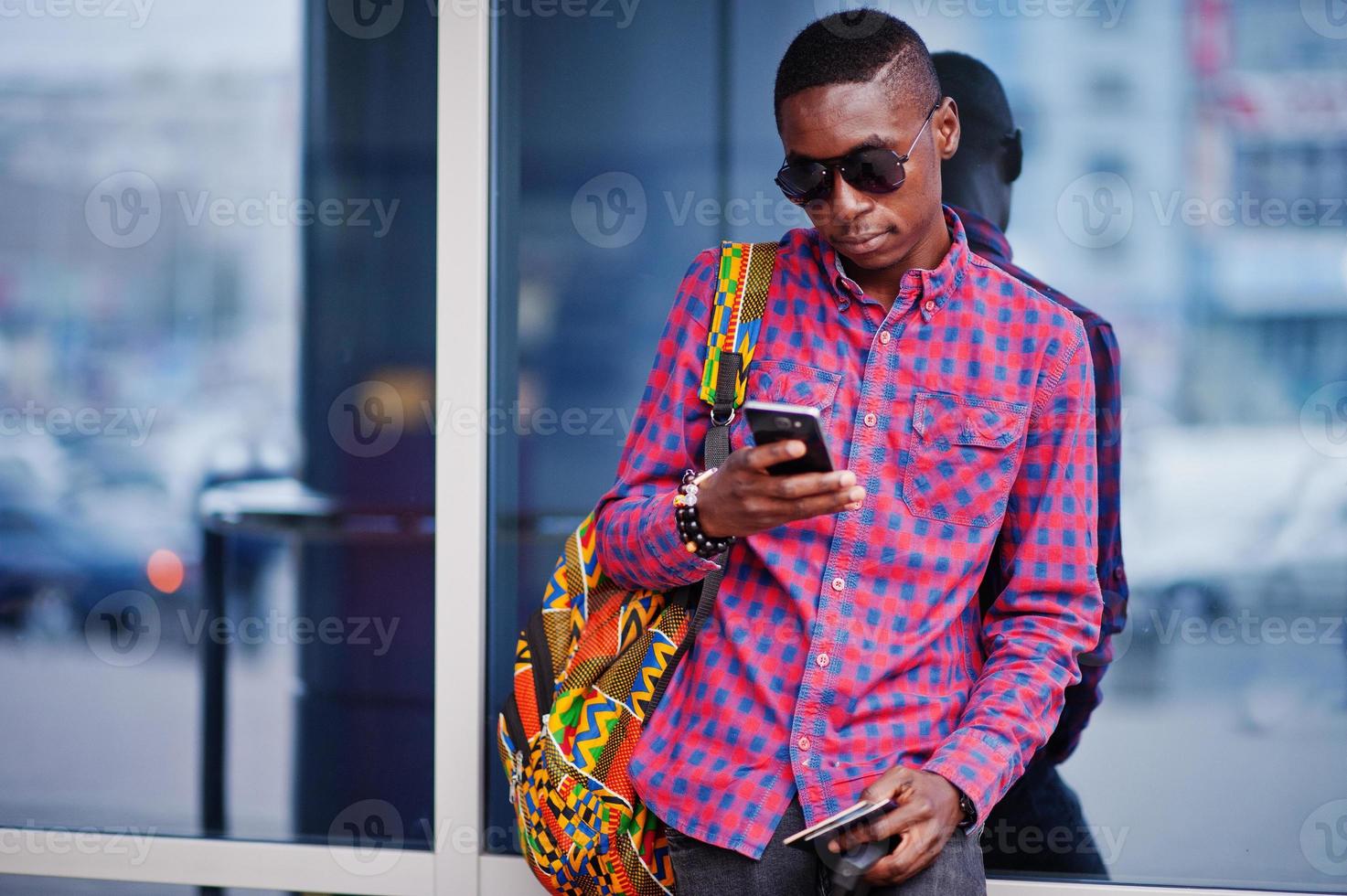 uomo afroamericano in camicia a scacchi, con valigia e zaino. viaggiatore nero contro la stazione degli autobus. foto