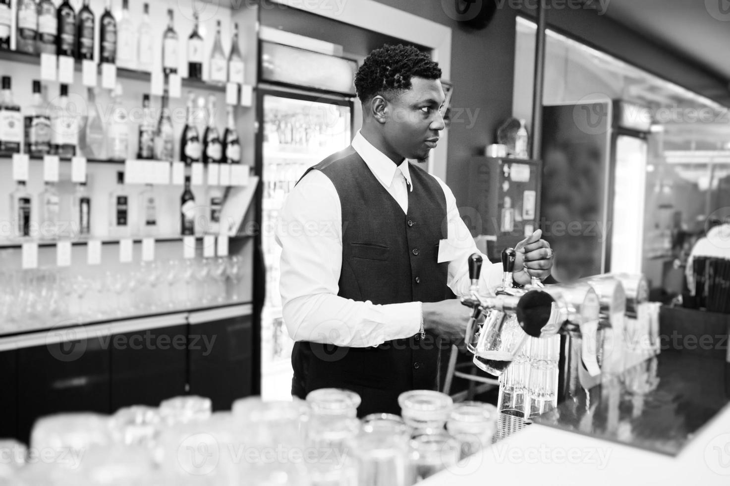 barista afroamericano al bar che versa dal rubinetto birra fresca nel bicchiere del pub. foto