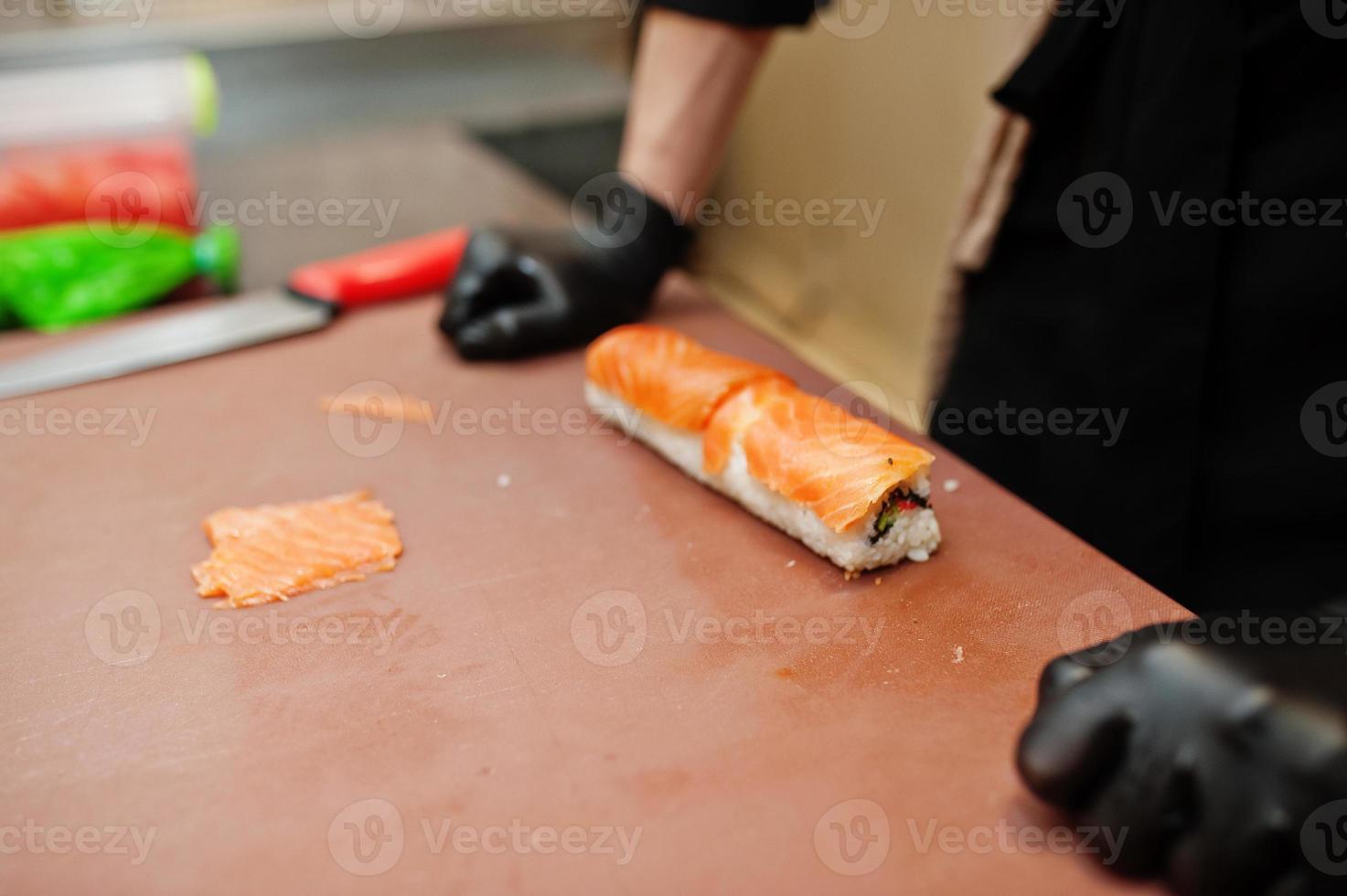 mani ravvicinate di chef professionisti indossano guanti neri che preparano sushi e panini in un ristorante cucina di cibo tradizionale giapponese. foto