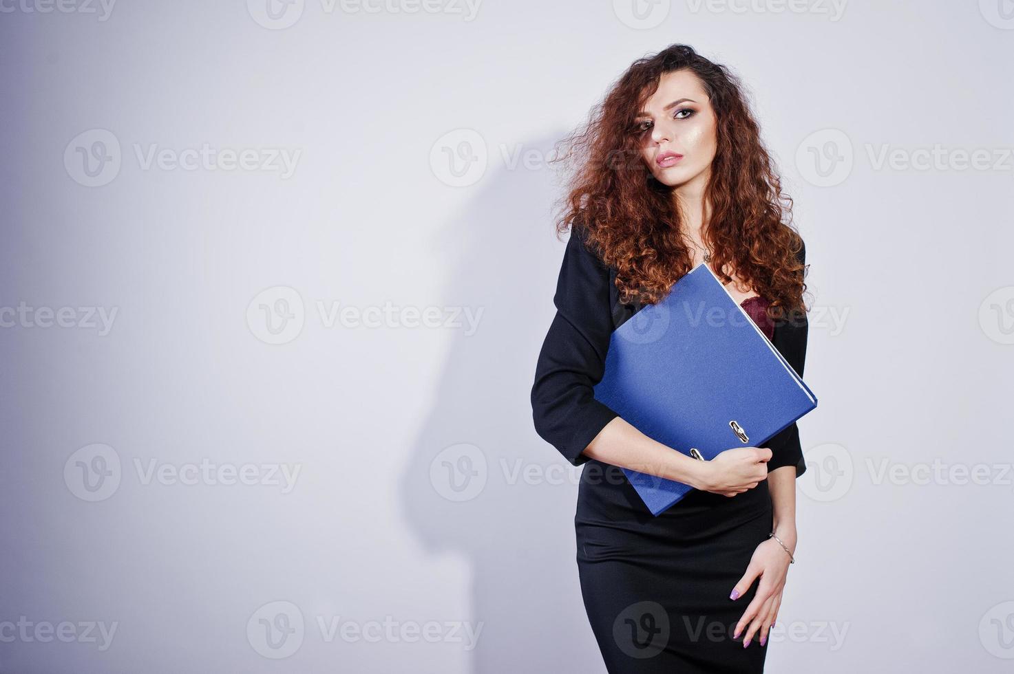 ragazza dai capelli ricci bruna in giacca da ufficio nera con gonna, sul reggiseno con cartella di documenti a portata di mano in studio su sfondo bianco. donna d'affari sexy. foto