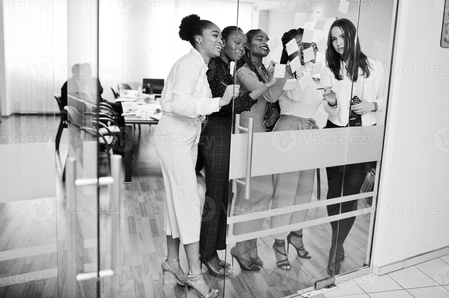 donna d'affari che punta su vetro con note di carta colorate. gruppo eterogeneo di dipendenti di sesso femminile in abiti formali che utilizzano adesivi. foto