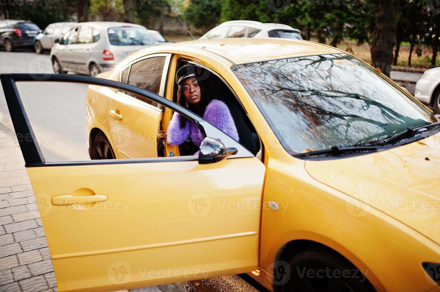 donna afroamericana in abito viola e berretto posati su un'auto gialla. foto