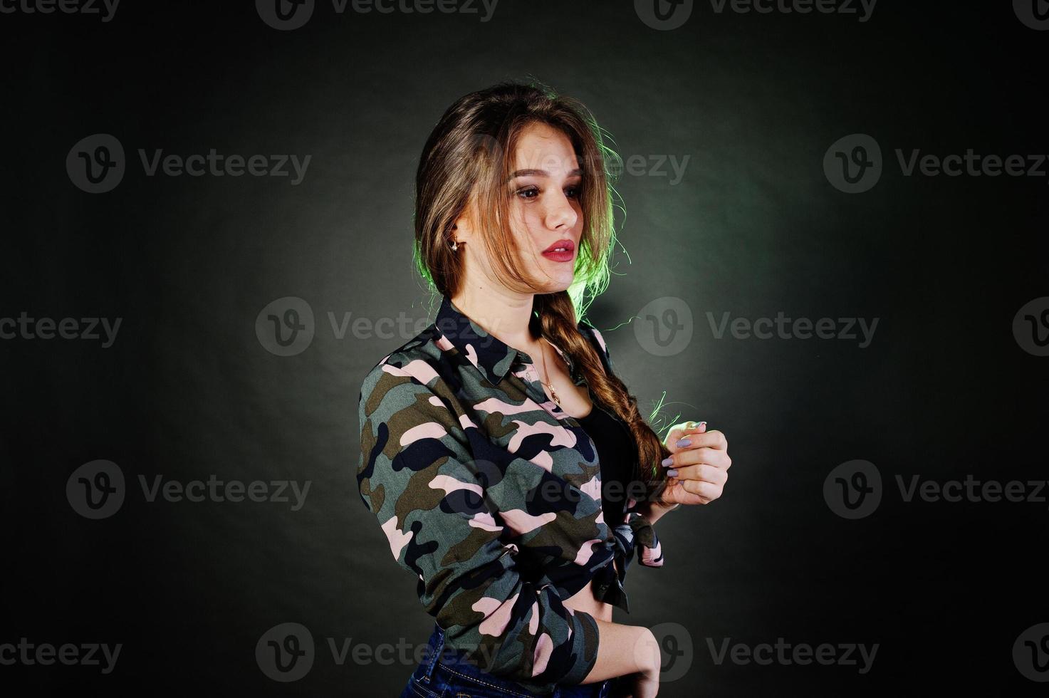 bella ragazza bruna indossare camicia militare e jeans, in posa in studio su sfondo grigio. ritratto del modello in studio. foto