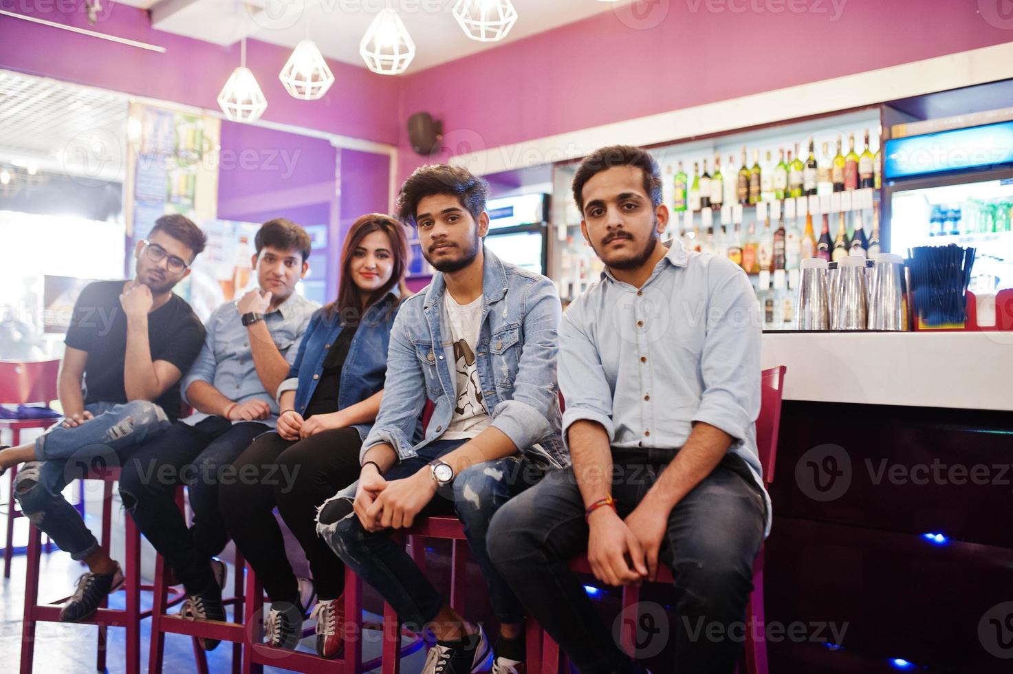 gruppo di amici asiatici alla moda indossano jeans seduti su sedie contro il bar nel club. foto