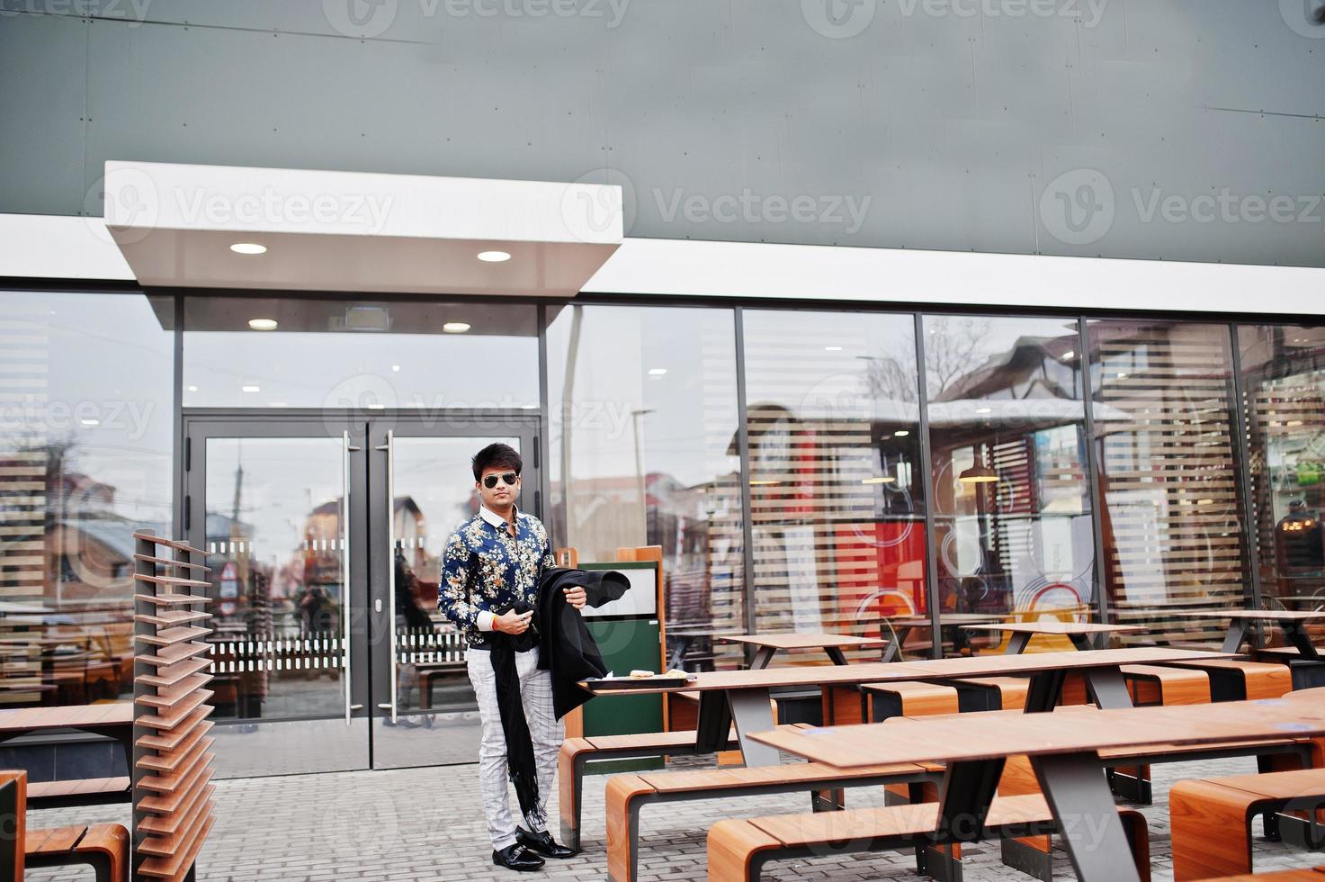 l'uomo indiano alla moda attraente e bello indossa camicia e occhiali da sole in piedi sulla terrazza del moderno lounge cafe durante la sua pausa di lavoro. foto