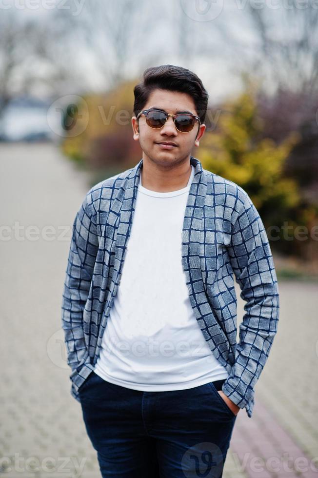 il giovane indiano alla moda con gli occhiali da sole indossa una posa casual all'aperto. foto