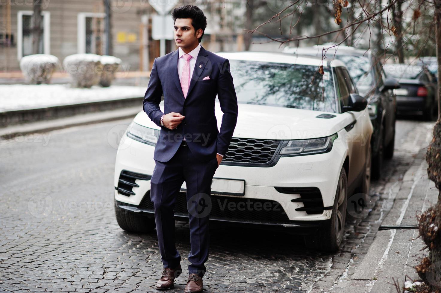 modello di uomo macho indiano elegante su abito e cravatta rosa in posa contro un'auto bianca da lavoro. foto