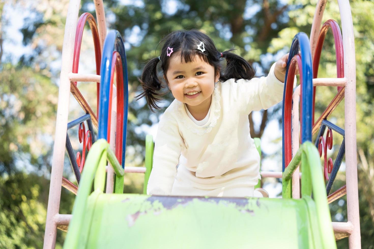 ragazza asiatica carina gioca a scuola o nel cortile dell'asilo o nel parco giochi. sana attività estiva per i bambini. piccola ragazza asiatica che si arrampica all'aperto al parco giochi. bambino che gioca nel parco giochi all'aperto. foto