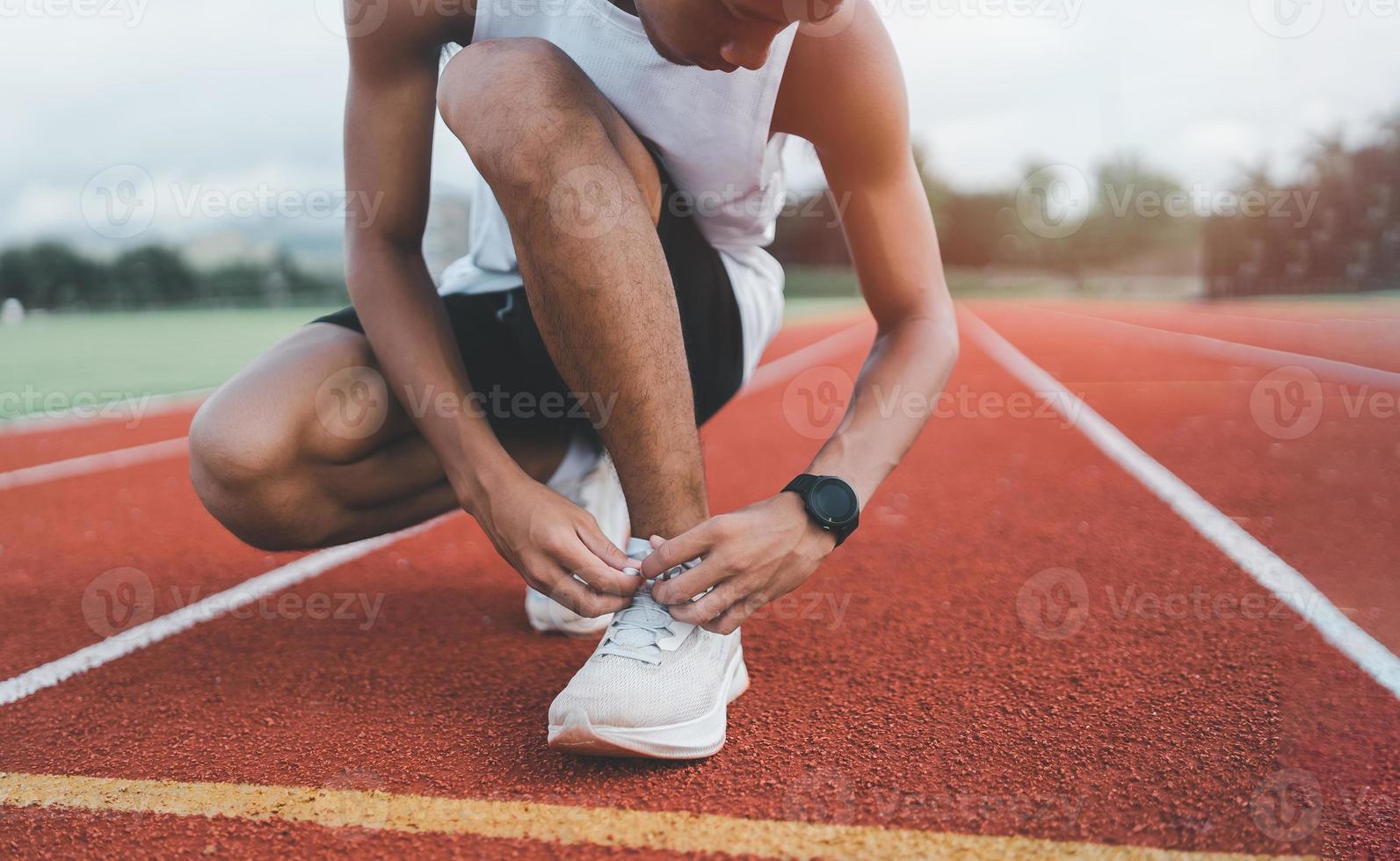 corridore uomo inginocchiato e legare il laccio delle scarpe sulla corsia dello stadio, atleta sportivo si prepara ad allenarsi per la gara di competizione. concetto di corsa sportiva. foto