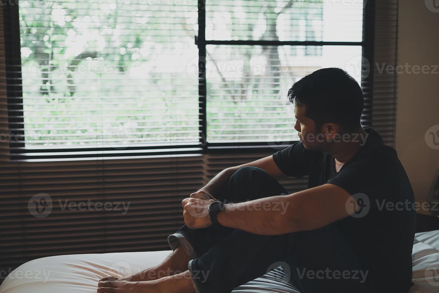 uomo asiatico triste che soffre di depressione insonnia sveglio e si siede da solo sul letto in camera da letto. silhouette uomo depresso tristemente seduto sul letto in camera da letto, concetto di depressione foto