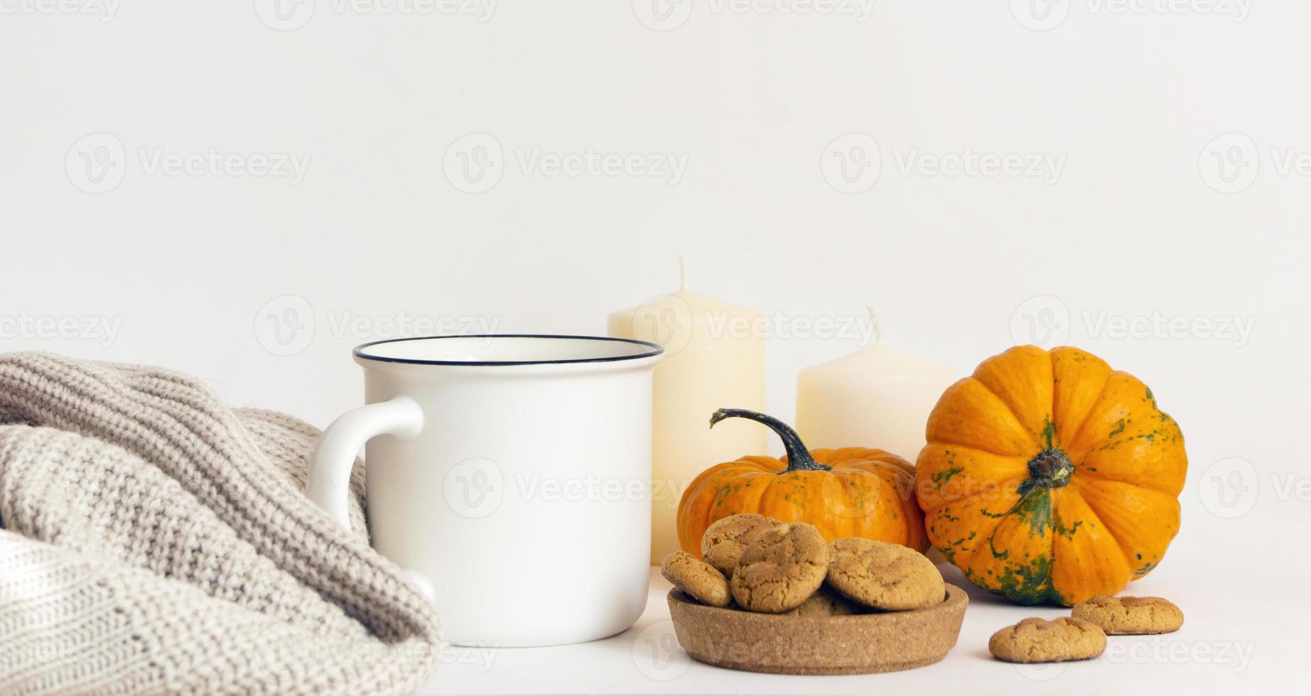 caffè mattutino, atmosfera autunnale. tazza, sciarpa, biscotti, zucche e candele su un tavolo bianco foto