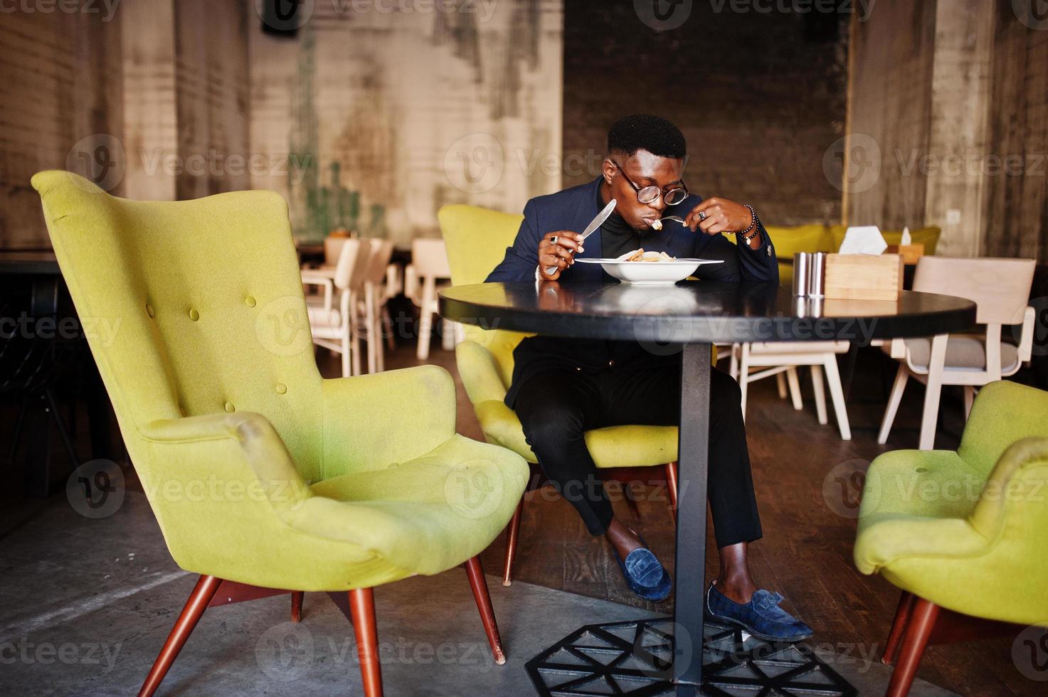 uomo afroamericano alla moda in giacca e occhiali seduto al bar e mangiare insalata. foto