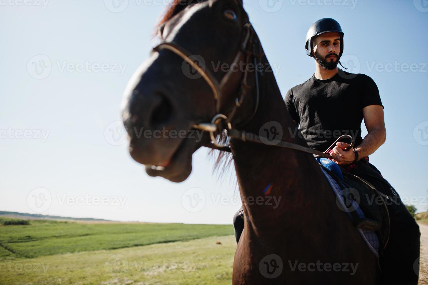 l'uomo arabo con barba alta indossa un casco nero, cavalca un cavallo arabo. foto