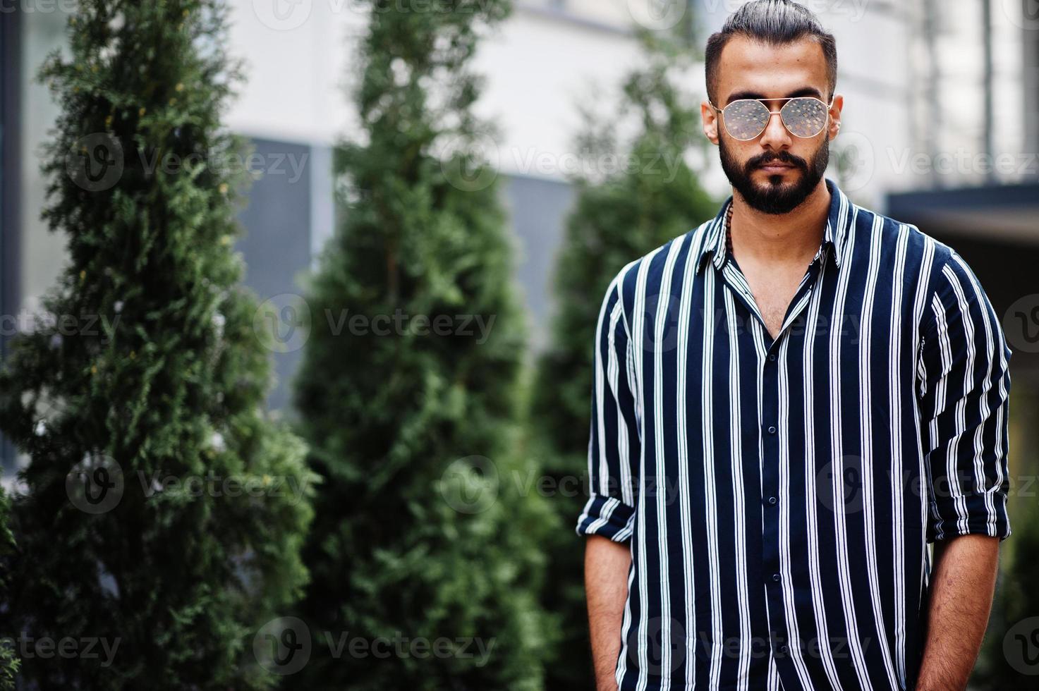 indossare uomo arabo di successo in camicia a righe e occhiali da sole posa all'aperto. foto