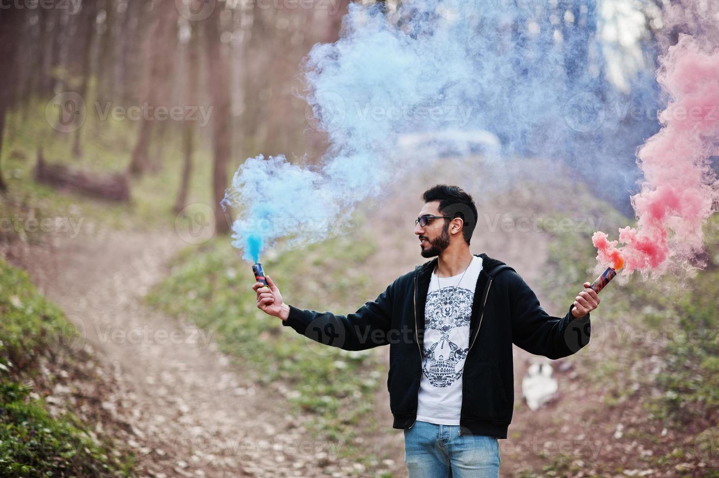 l'uomo arabo di street style con gli occhiali tiene il bagliore della mano con una bomba fumogena rossa e blu. foto