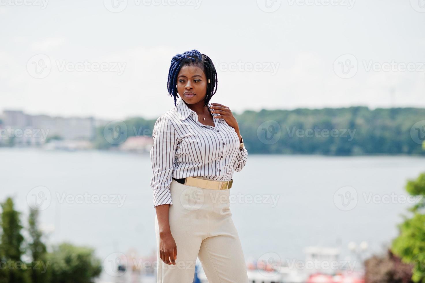 elegante donna d'affari afroamericana in pantaloni e camicetta poste all'aperto contro il lago. foto