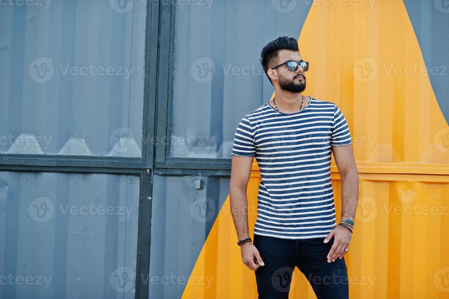 bel modello uomo alto con barba araba in camicia spogliata in posa all'aperto. ragazzo arabo alla moda con occhiali da sole contro il muro dipinto di giallo. foto