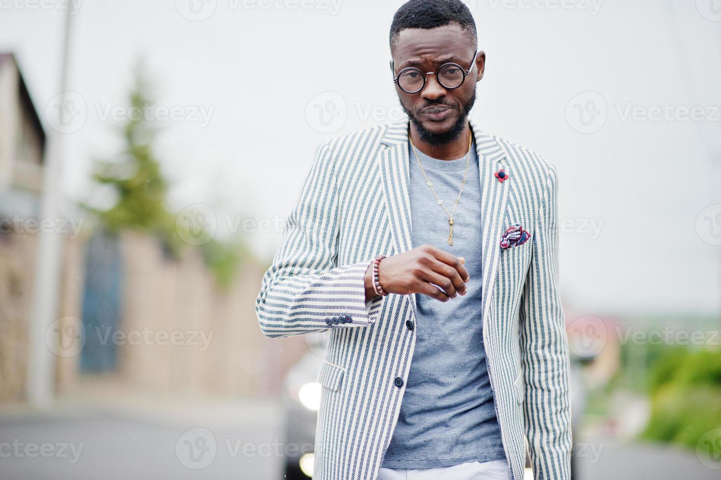 uomo afroamericano ricco ed elegante in giacca e pantaloni bianchi, occhiali in posa. foto