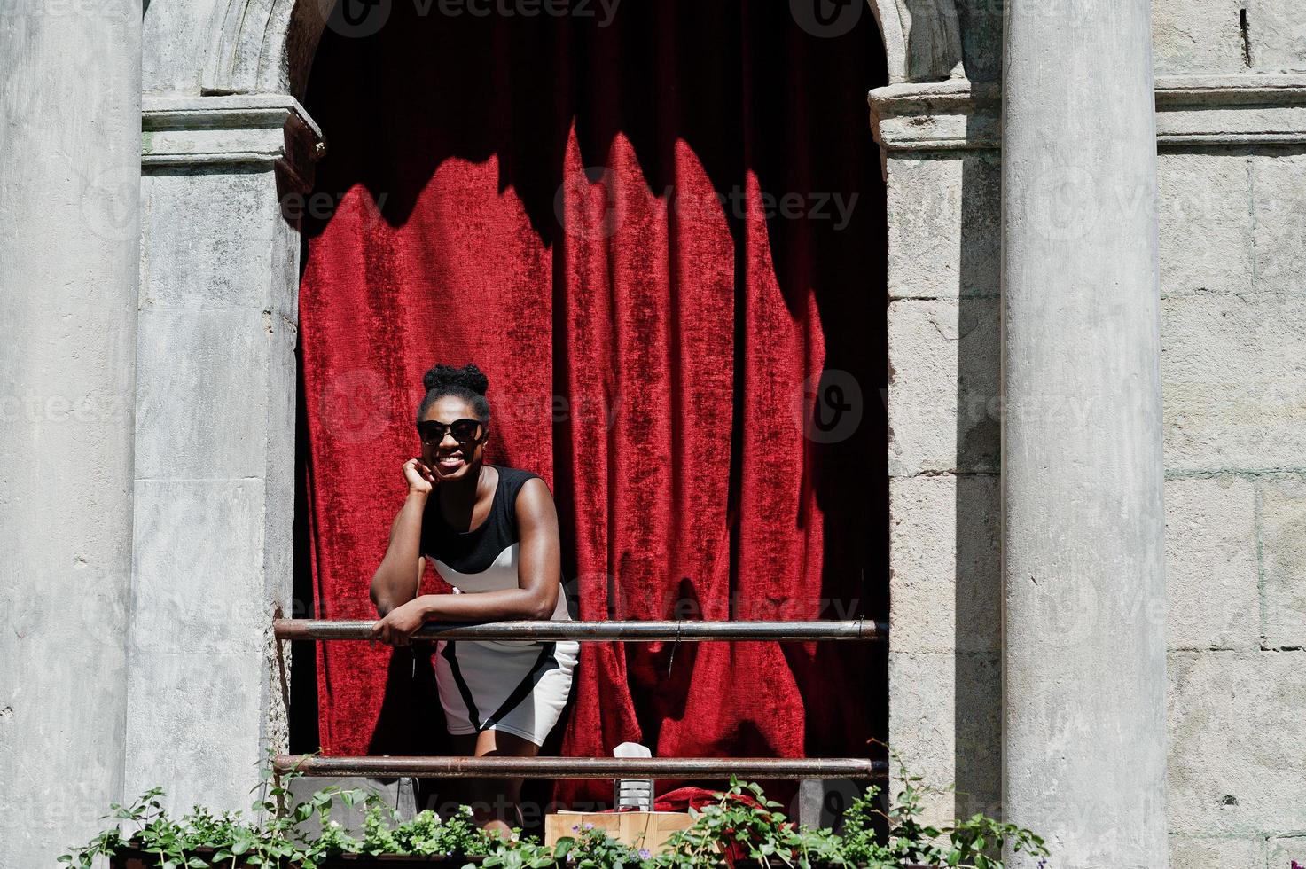 elegante donna afroamericana posata al balcone con tenda rossa all'aperto. foto