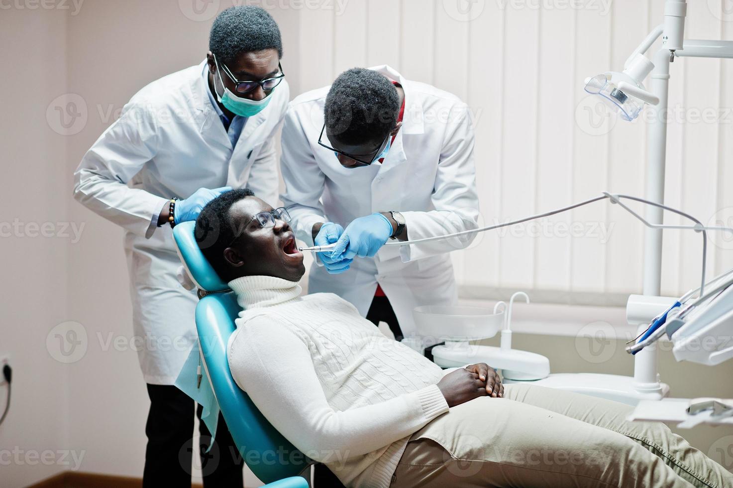 paziente uomo afroamericano in poltrona odontoiatrica. studio dentistico e concetto di pratica medica. dentista professionista che aiuta il suo paziente in odontoiatria medica. perforazione dei denti del paziente in clinica. foto