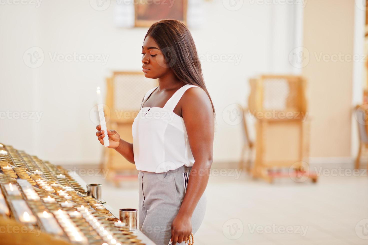 donna afroamericana che prega nella chiesa. i credenti meditano nella cattedrale e nel tempo spirituale della preghiera. ragazza afro con le candele. foto