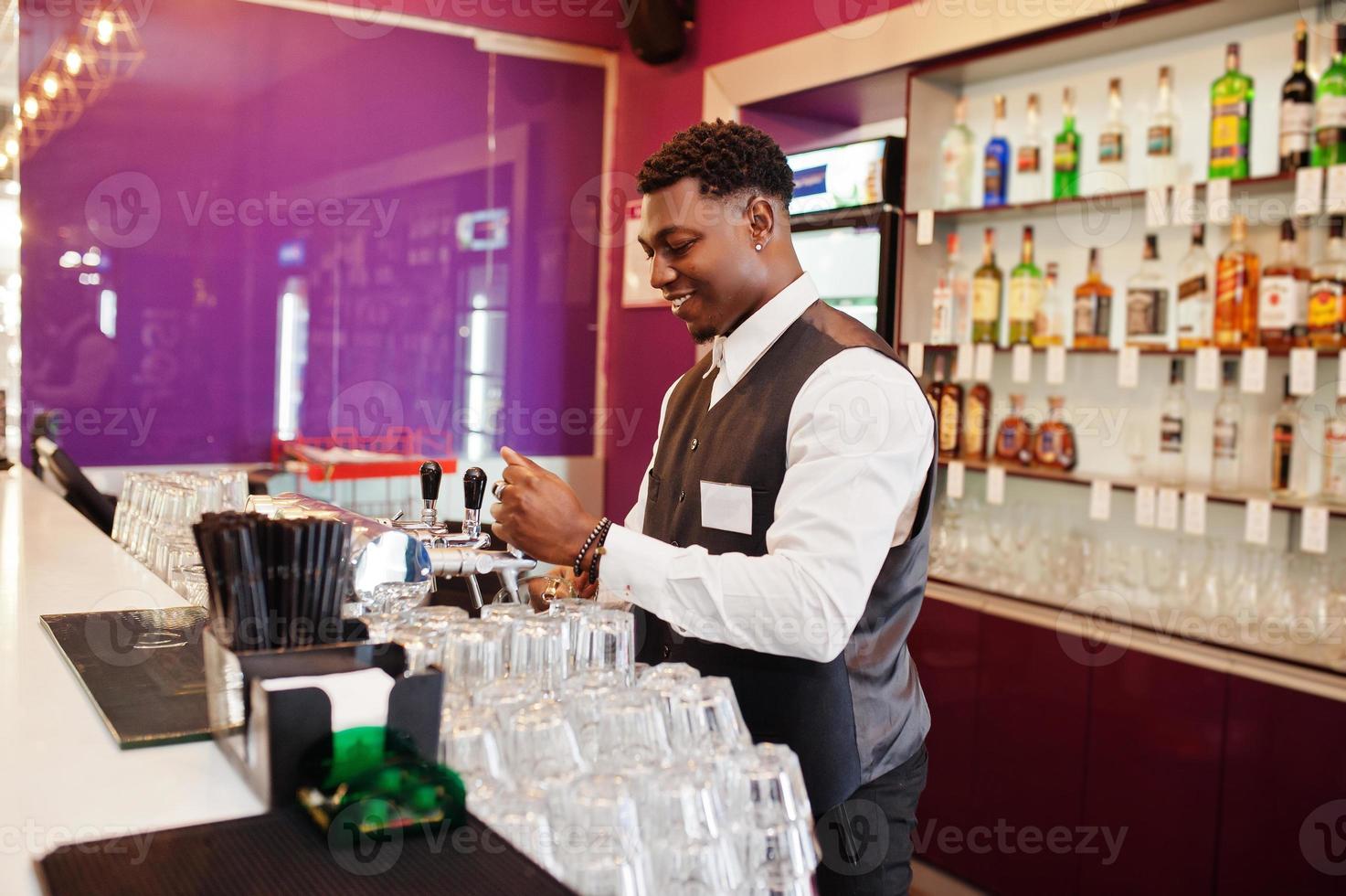 barista afroamericano al bar che versa dal rubinetto birra fresca nel bicchiere del pub. foto