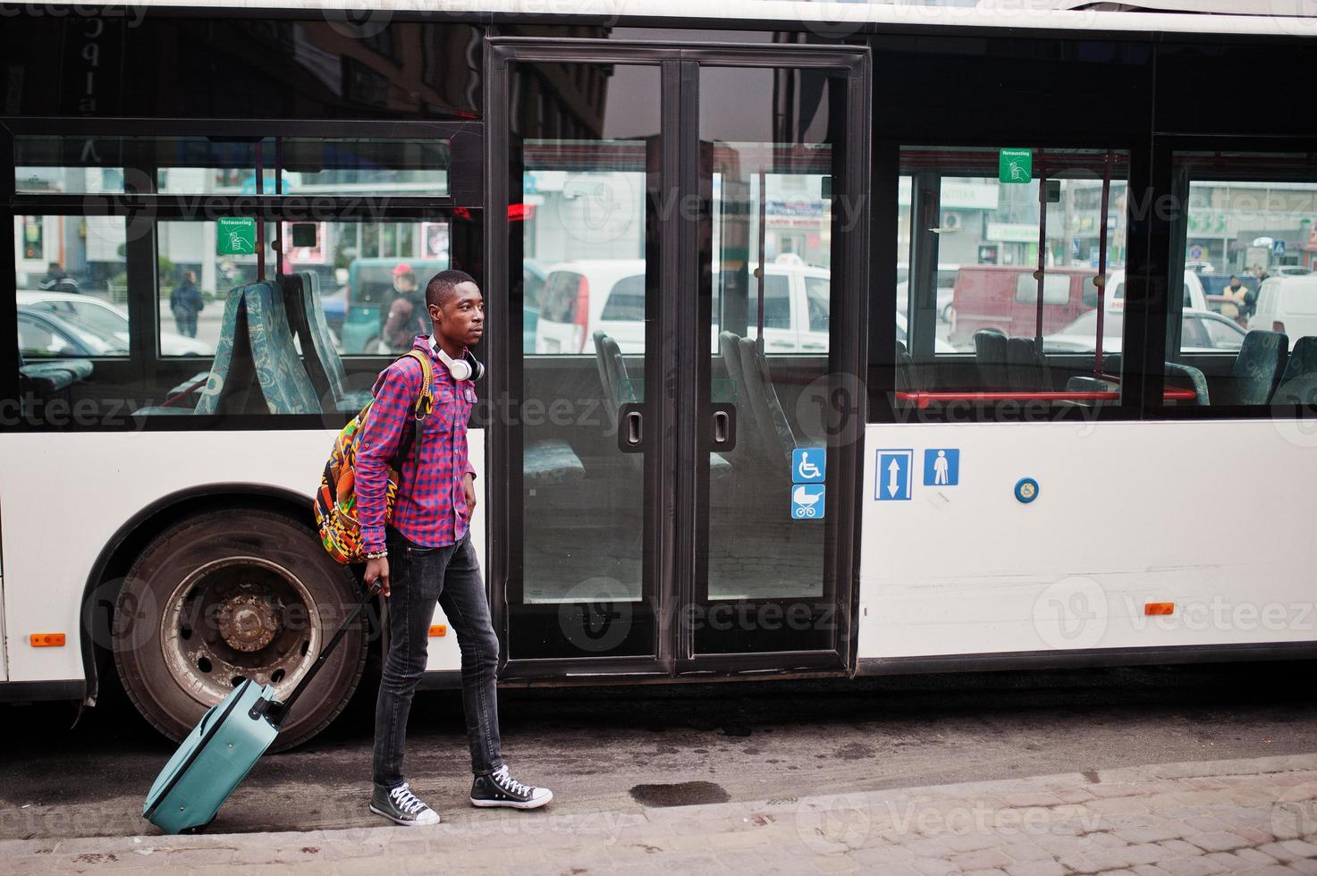 uomo afroamericano in camicia a scacchi, con valigia e zaino. viaggiatore nero contro autobus. foto