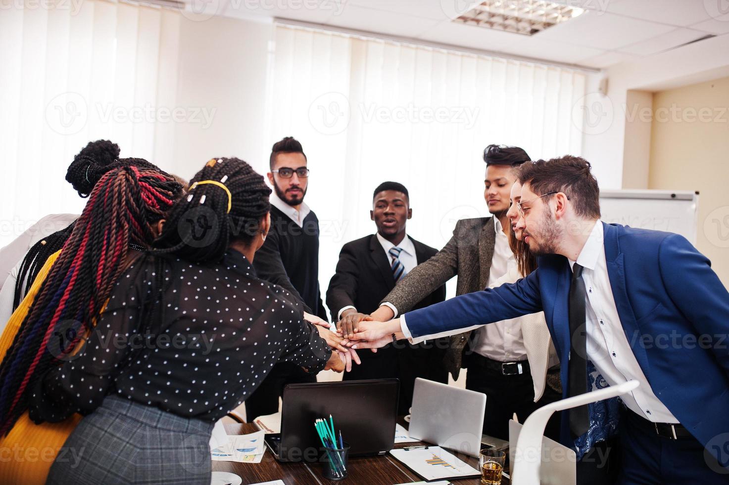 uomini d'affari multirazziali in piedi in ufficio e mettere le mani sulle mani. gruppo eterogeneo di dipendenti in abiti formali. foto