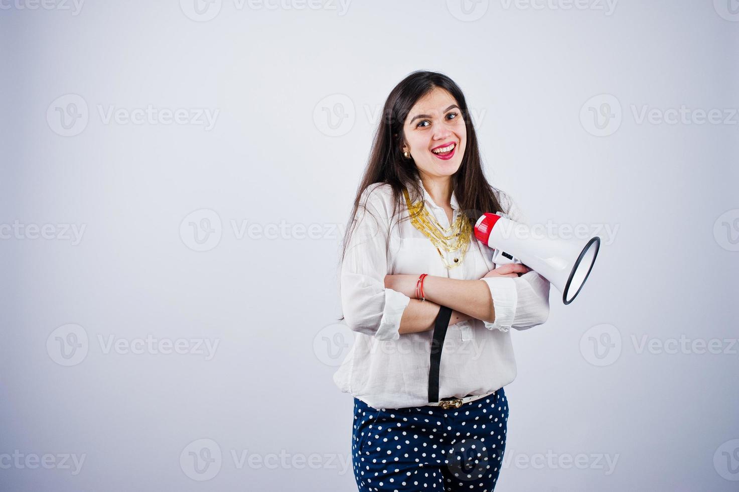 ritratto di una giovane donna in pantaloni blu e camicetta bianca in posa con il megafono in studio. foto