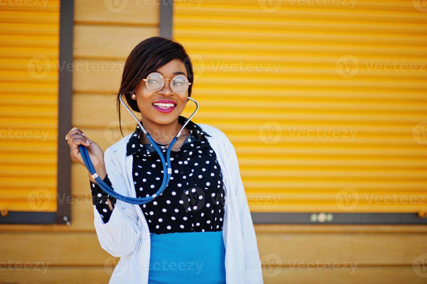 medico afroamericano femmina con stetoscopio posato sfondo esterno otturatore giallo. foto