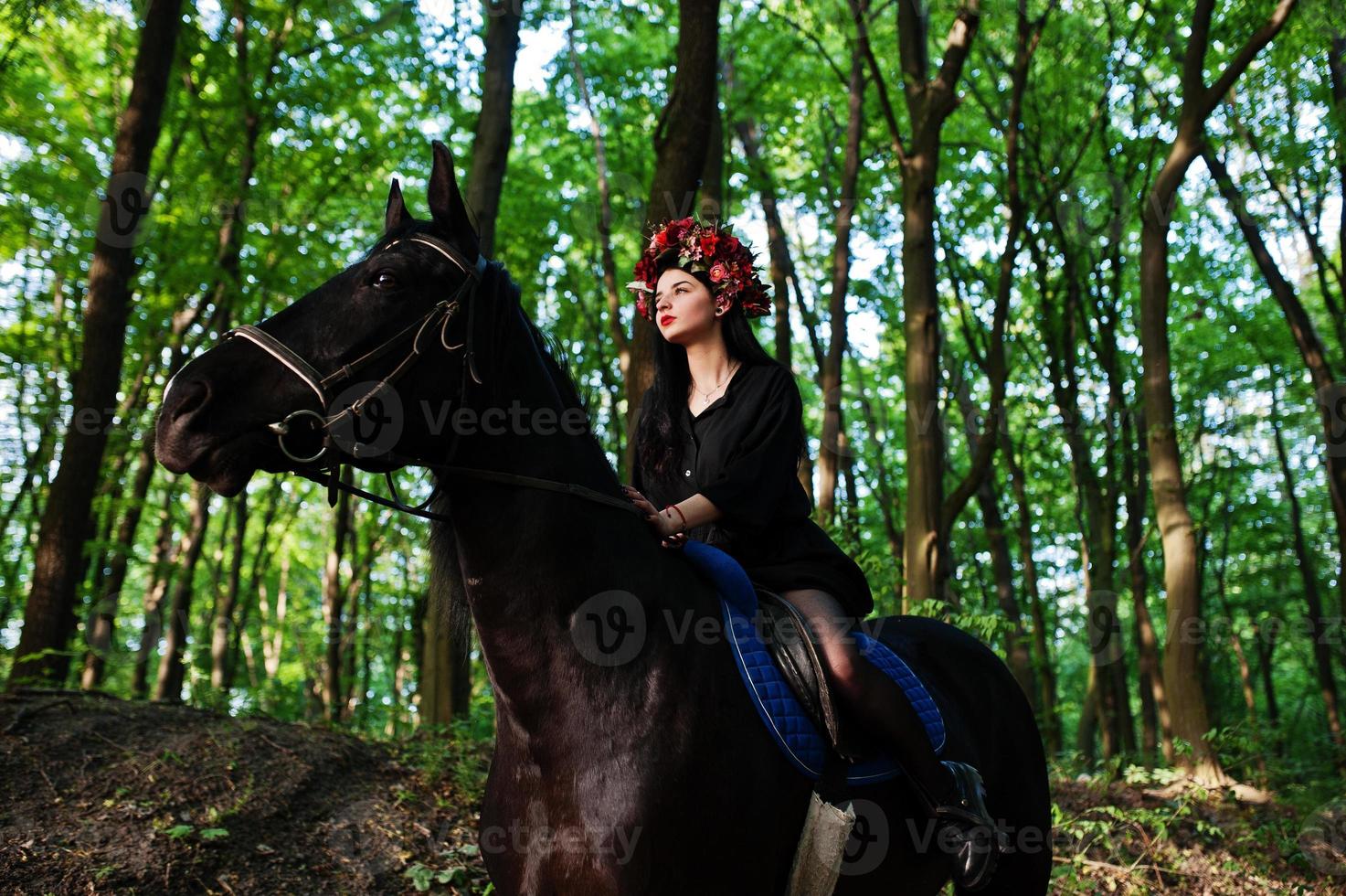 ragazza mistica in ghirlanda indossata in nero a cavallo in legno. foto