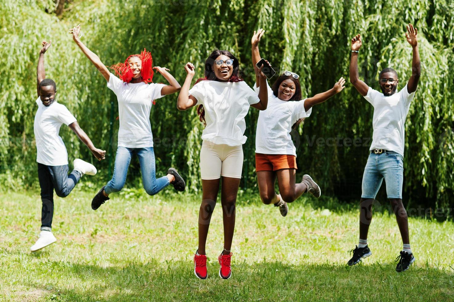 gruppo di persone afroamericane che saltano nel parco con magliette bianche. foto