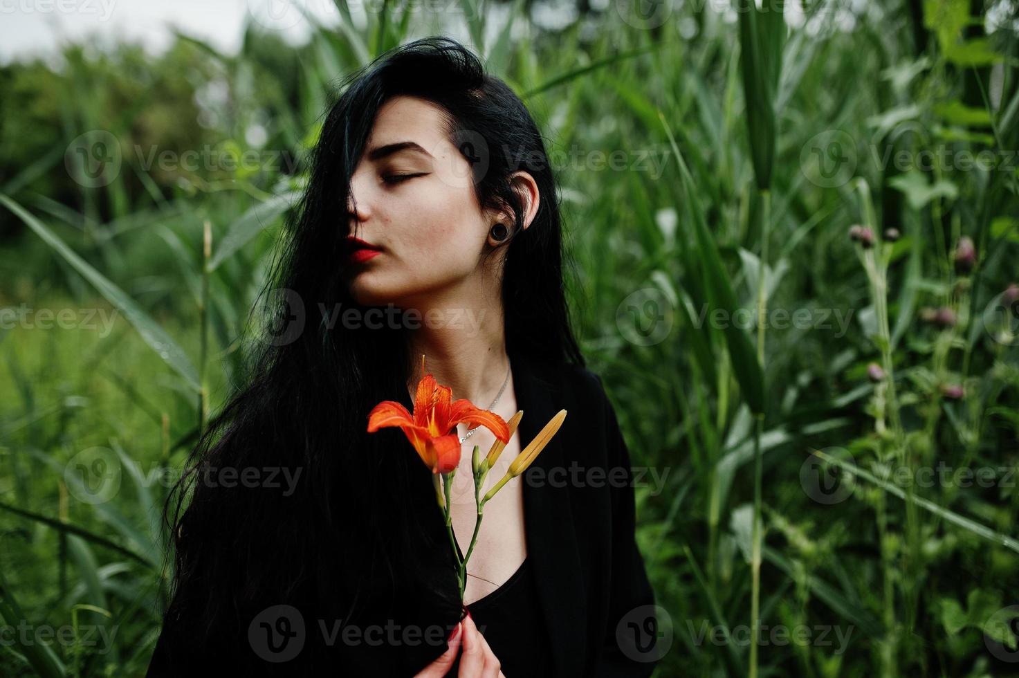 ragazza sensuale tutta in labbra rosse e nere. goth donna drammatica tenere fiore di giglio arancione su canna comune. foto