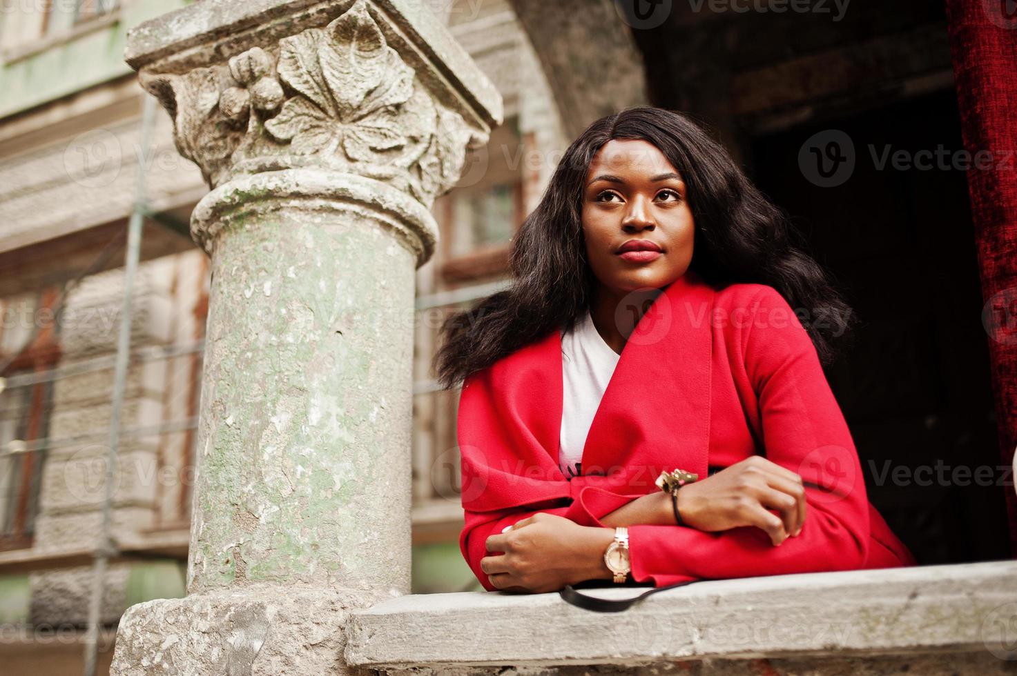 elegante donna afroamericana in cappotto rosso posata contro vecchie colonne. foto