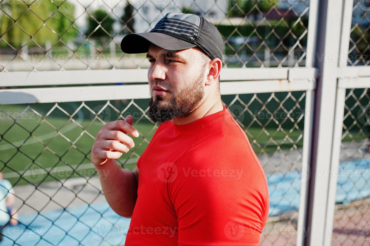 giovane uomo muscoloso barbuto brutale indossa maglietta rossa, pantaloncini e berretto allo stadio. foto