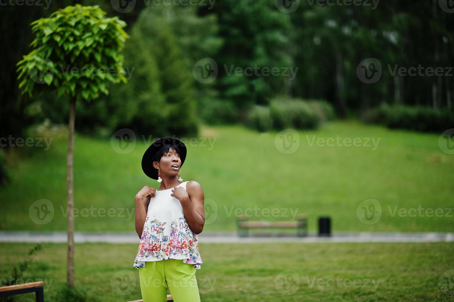 incredibile donna modello afroamericano in pantaloni verdi e cappello nero in posa al parco. foto