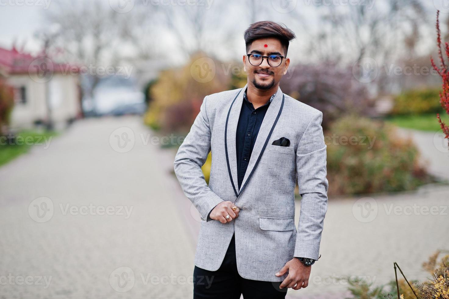 elegante uomo indiano con bindi sulla fronte e occhiali, indossa un abito posato all'aperto. foto